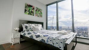 Une chambre moderne avec un grand lit, une table de chevet et une vue sur la ville grâce à une grande fenêtre.