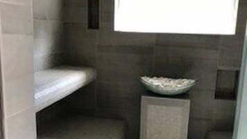 Modern bathroom with a curved bench, rectangular mirror, and light-colored tile floor.