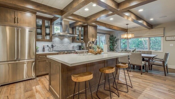 Een ruime keuken met een groot schiereiland, houten barstoelen en een eethoek met uitzicht op de omgeving.
