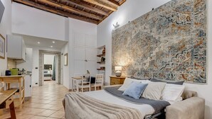 A bedroom with a large bed, a wooden desk, a chair, a wardrobe, and a wall with a patterned tapestry. - Coliseum Rome Apartments - Suite (Roma)
