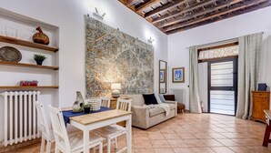 A living room with a dining table, chairs, a sofa, a large abstract painting, and a window with curtains. - Coliseum Rome Apartments - Suite (Roma)