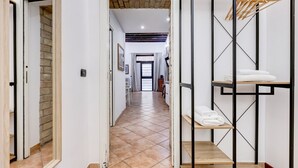 A hallway with a tiled floor, a wooden bench, a metal rack with towels, and a brick wall. - Coliseum Rome Apartments - Suite (Roma)