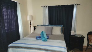 A neatly made bed with striped bedding, a lamp, and a chair in a room with curtains and a tiled floor. - Sagusta Gardens NCA 1 (Whitby)
