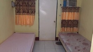 Eine kleine, einfache Unterkunft mit einem Bett, einer Tür und einem Fenster mit gemusterten Vorhängen.