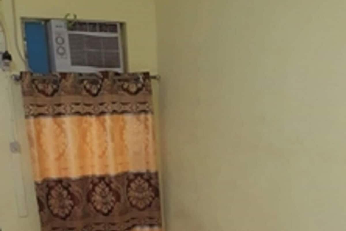 A small, single-bed room with a patterned bedspread, a window with a curtain, and a tiled floor.