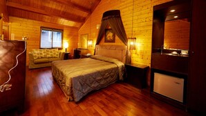 A cozy bedroom with a large bed, a small sofa, a vanity with a mirror, and a refrigerator. - New Era Art Resort & Spa (Puli)