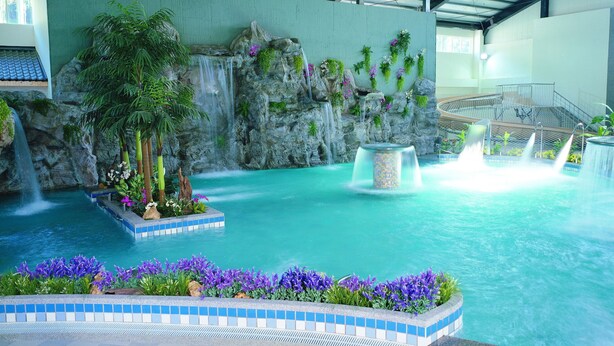 An indoor pool with a waterfall, surrounded by tropical plants and flowers. - New Era Art Resort & Spa (Puli)