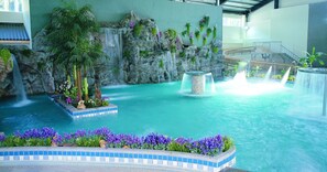 An indoor pool with a waterfall, surrounded by tropical plants and flowers. - New Era Art Resort & Spa (Puli)