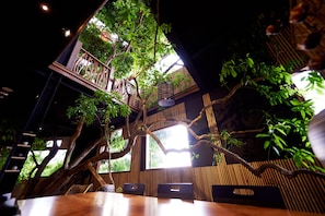A restaurant with a high ceiling, wooden beams, and a large tree in the center. - New Era Art Resort & Spa (Puli)