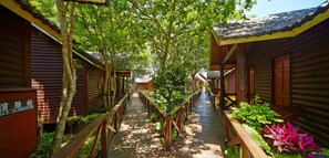 A wooden corridor with a wooden walkway flanked by log cabins, surrounded by lush greenery. - New Era Art Resort & Spa (Puli)
