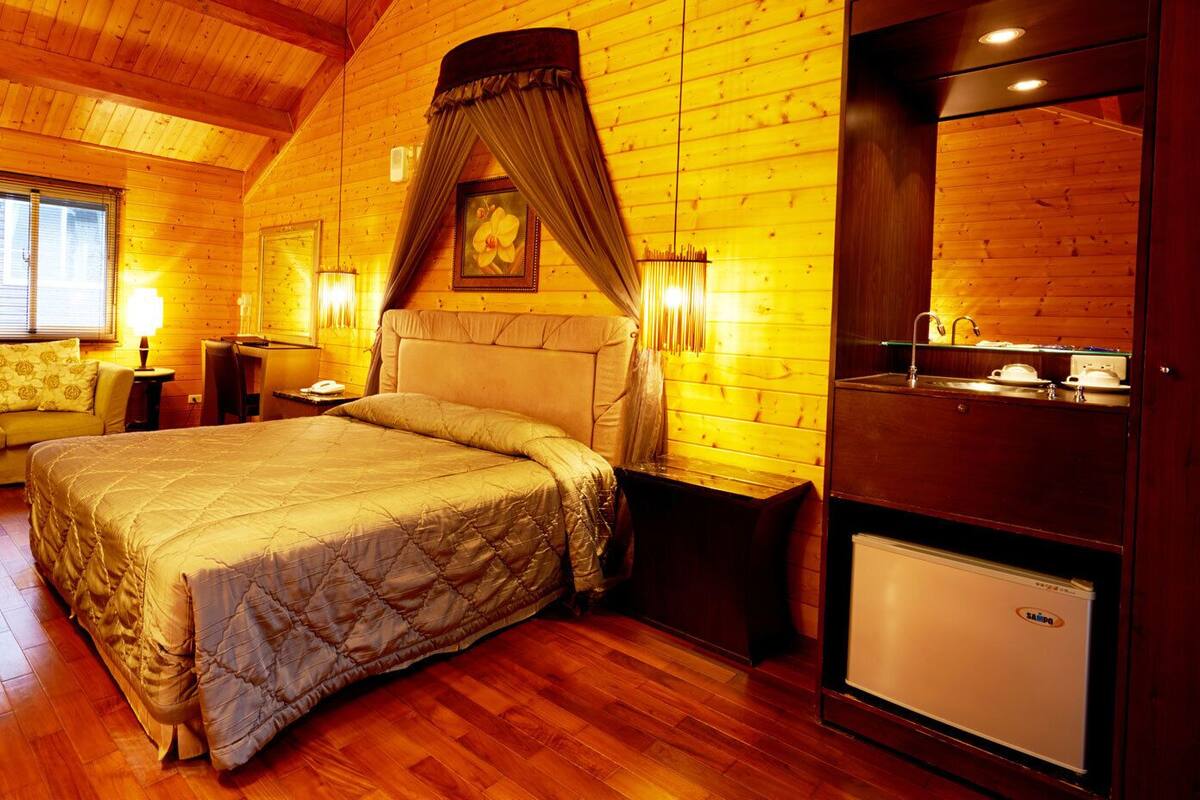 Um quarto aconchegante com uma cama grande, um sofá, uma toucador com espelho e uma geladeira.