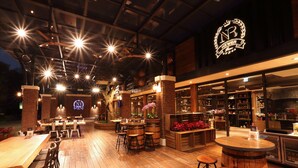An indoor restaurant with wooden flooring, bar stools, and tables. There are illuminated signs and a large logo on the wall. - New Era Art Resort & Spa (Puli)