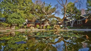 A serene lakeside setting with a wooden cabin, a pond with lily pads, and surrounding trees. - New Era Art Resort & Spa (Puli)