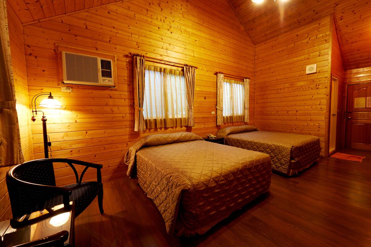 Quarto de cabana de madeira com duas camas, uma cadeira e um abajur.