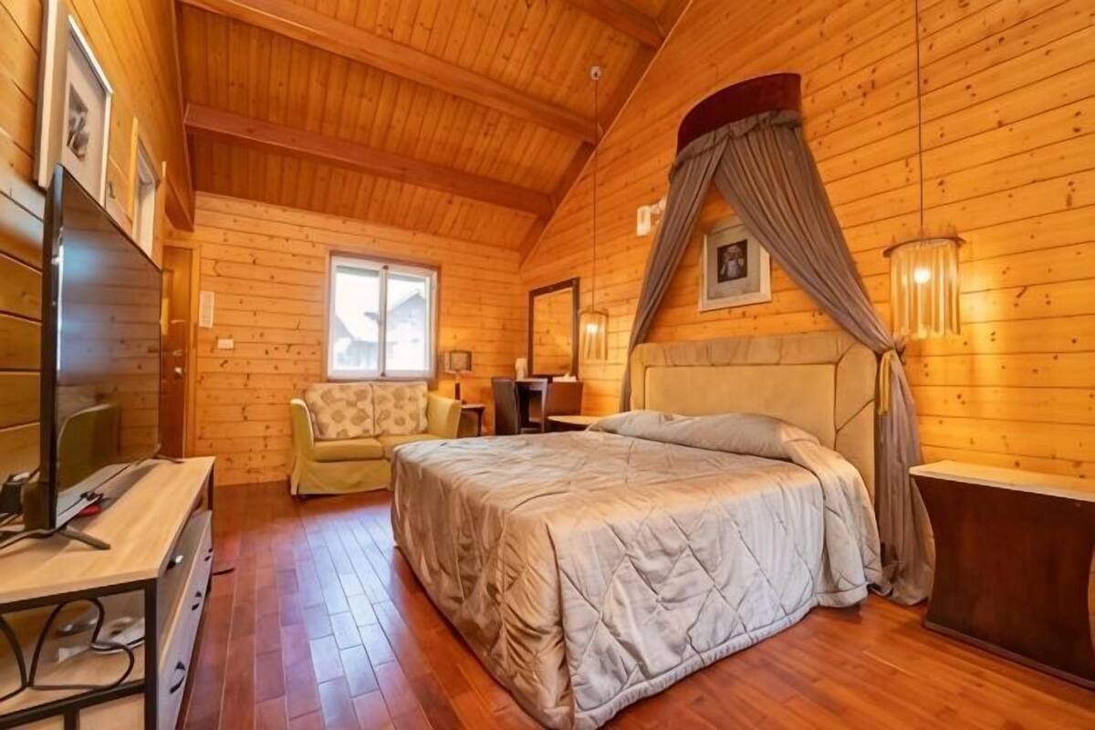 Quarto de cabana de madeira com cama, escrivaninha, cadeira e janela.