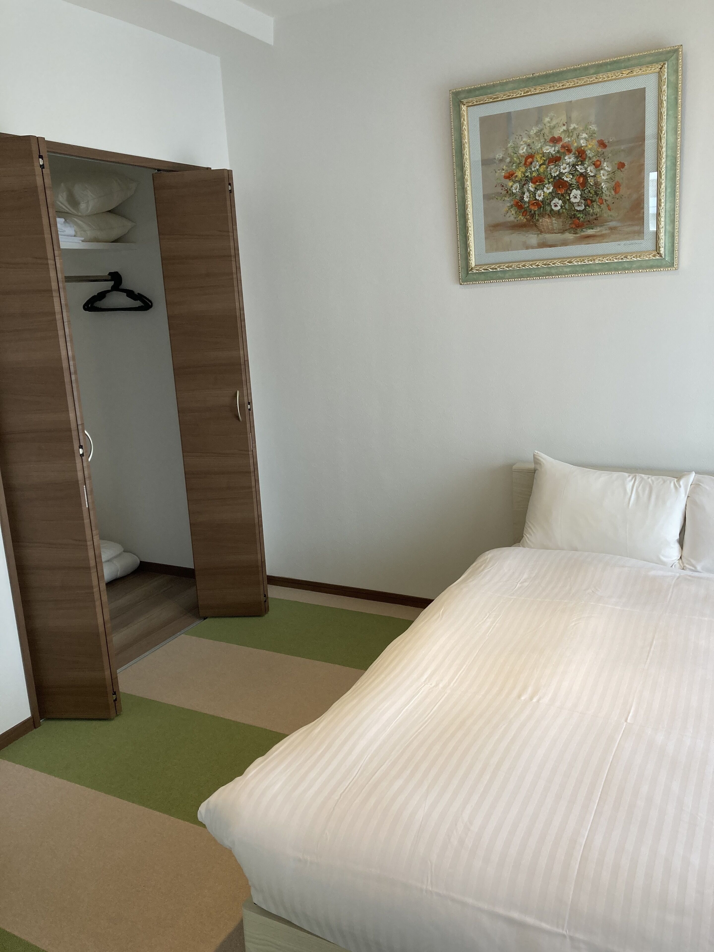 A hotel room with a bed, a wardrobe, and a framed picture on the wall.