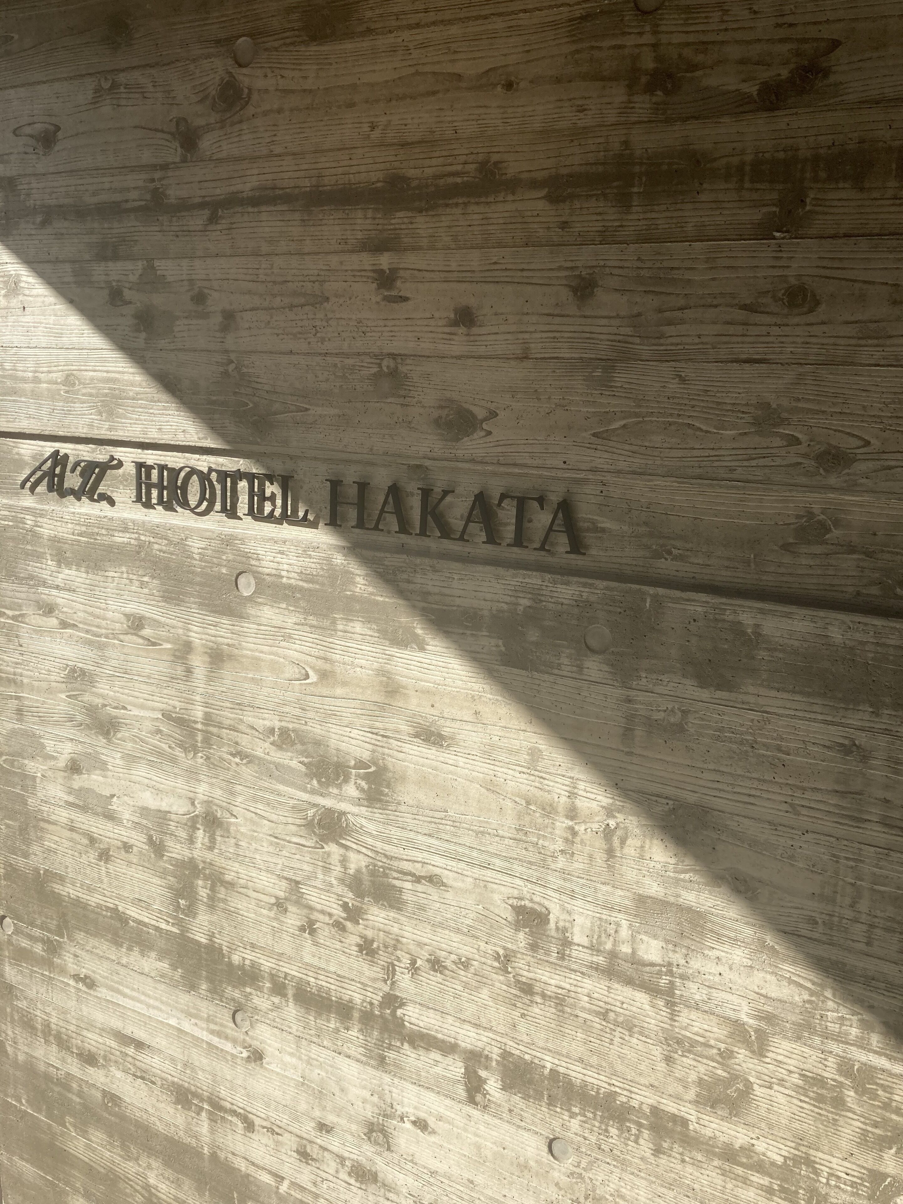 A wooden wall with the text "AZ HOTEL HAKATA" engraved on it.