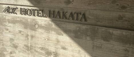 A wooden wall with the text "AZ HOTEL HAKATA" engraved on it.