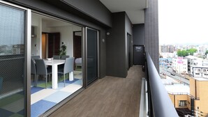 A balcony with a dining area, a sliding glass door leading to a room, and a city view. - A.T. Hotel Hakata (Fukuoka)