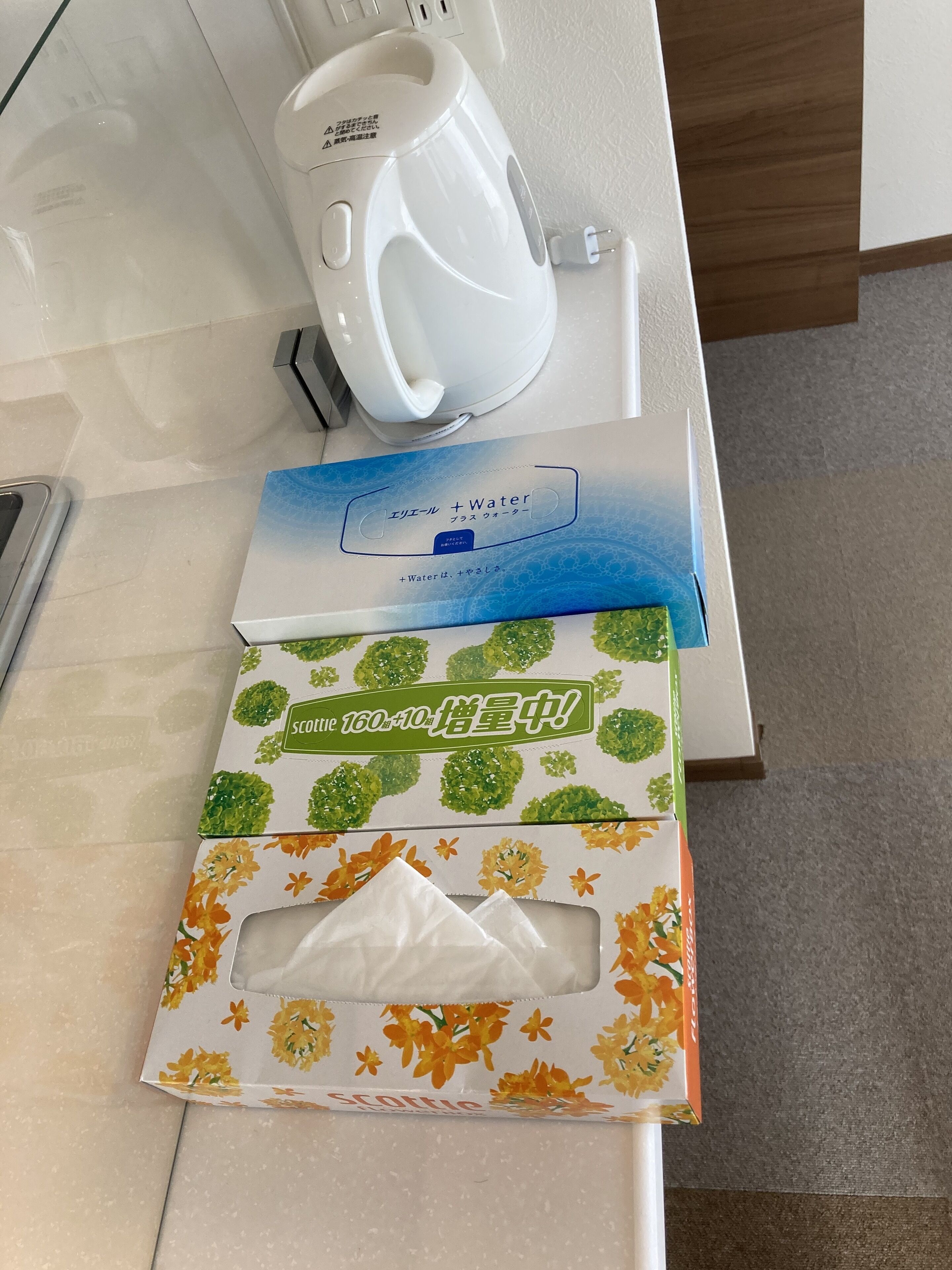 Eine Arbeitsplatte mit einem weißen Wasserkocher, einer Scotch-Tape-Kartusche und einer Packung Taschentücher.
