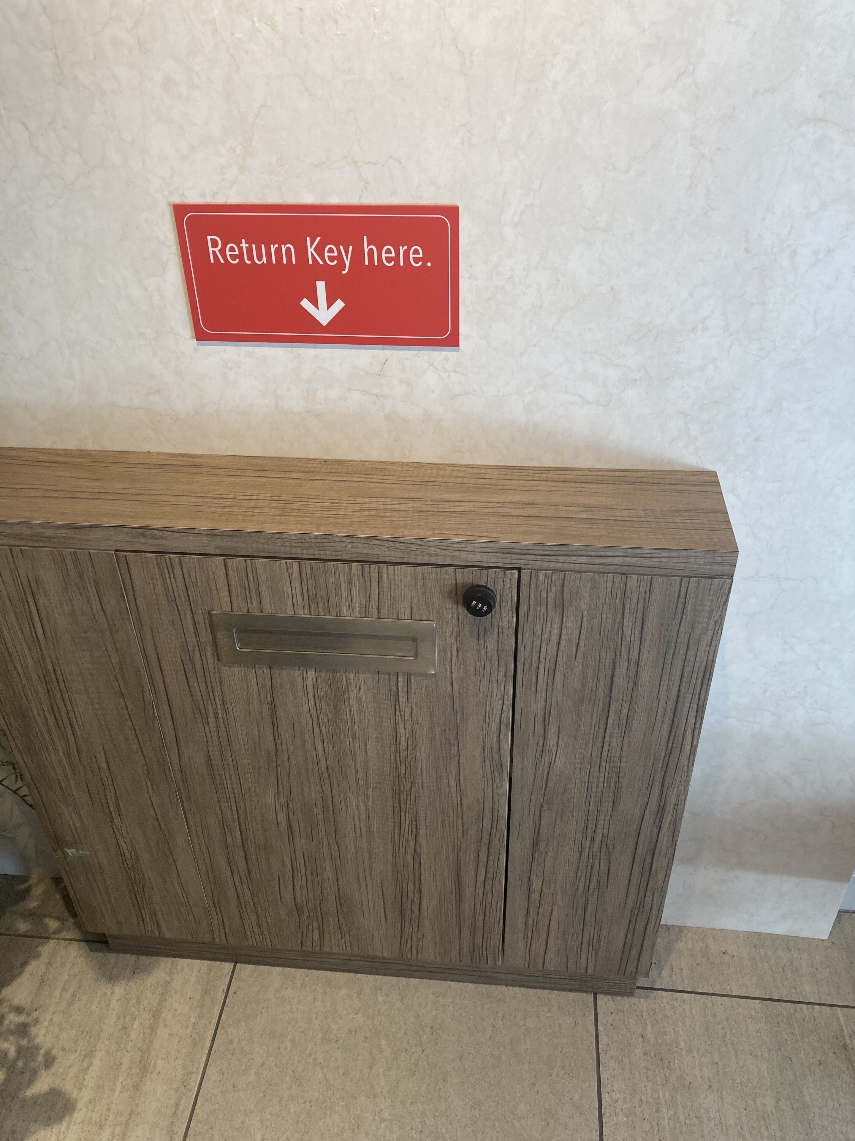 A wooden cabinet with a metal handle and a red sign above it that reads "Return Key here."