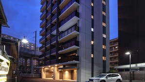 A multi-story hotel with a modern design, featuring balconies on each floor and a parking area in front. - A.T. Hotel Hakata (Fukuoka)