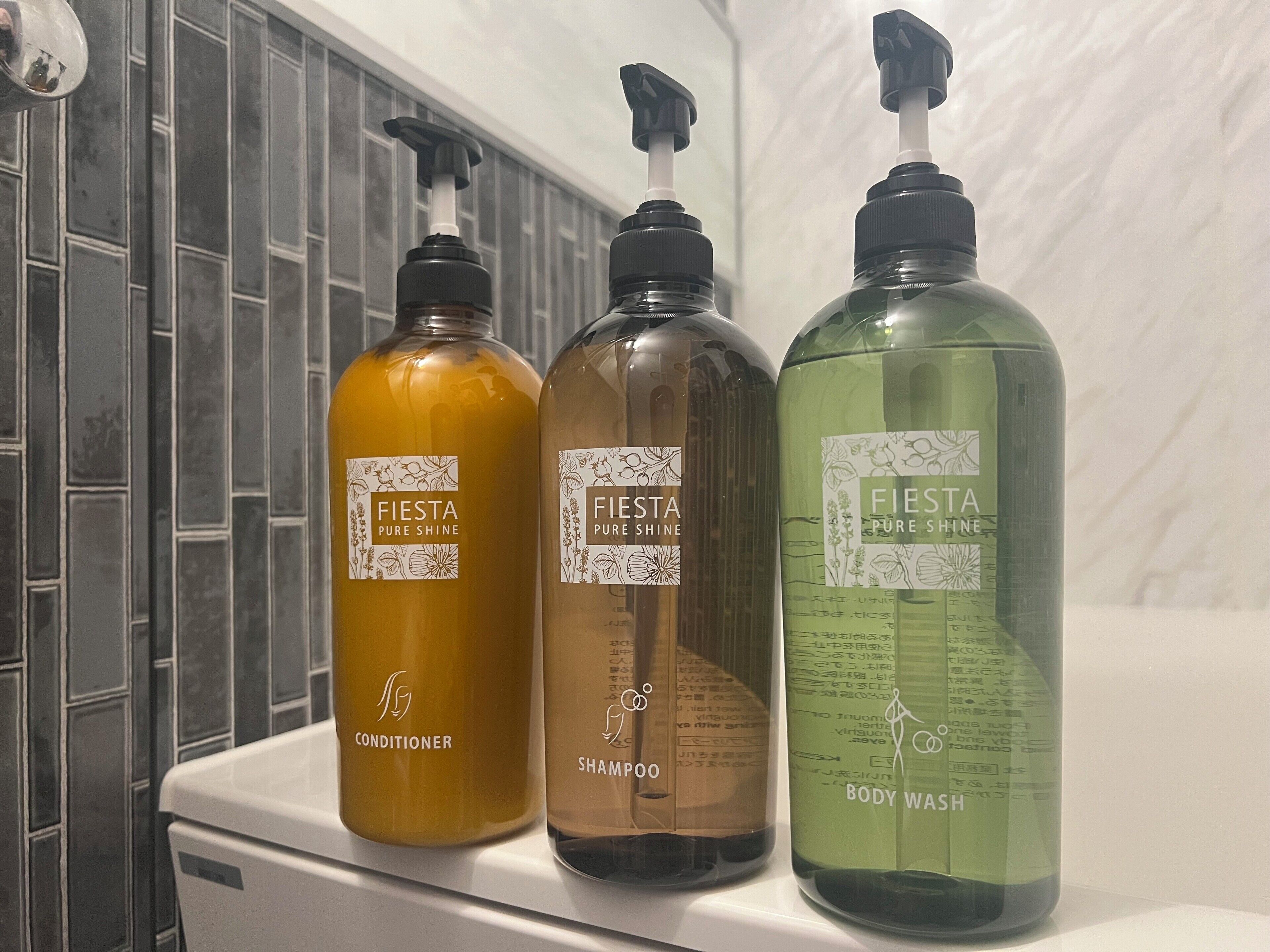 Three bottles of Fiesta Pure Shine products: conditioner, shampoo, and body wash, on a white surface.