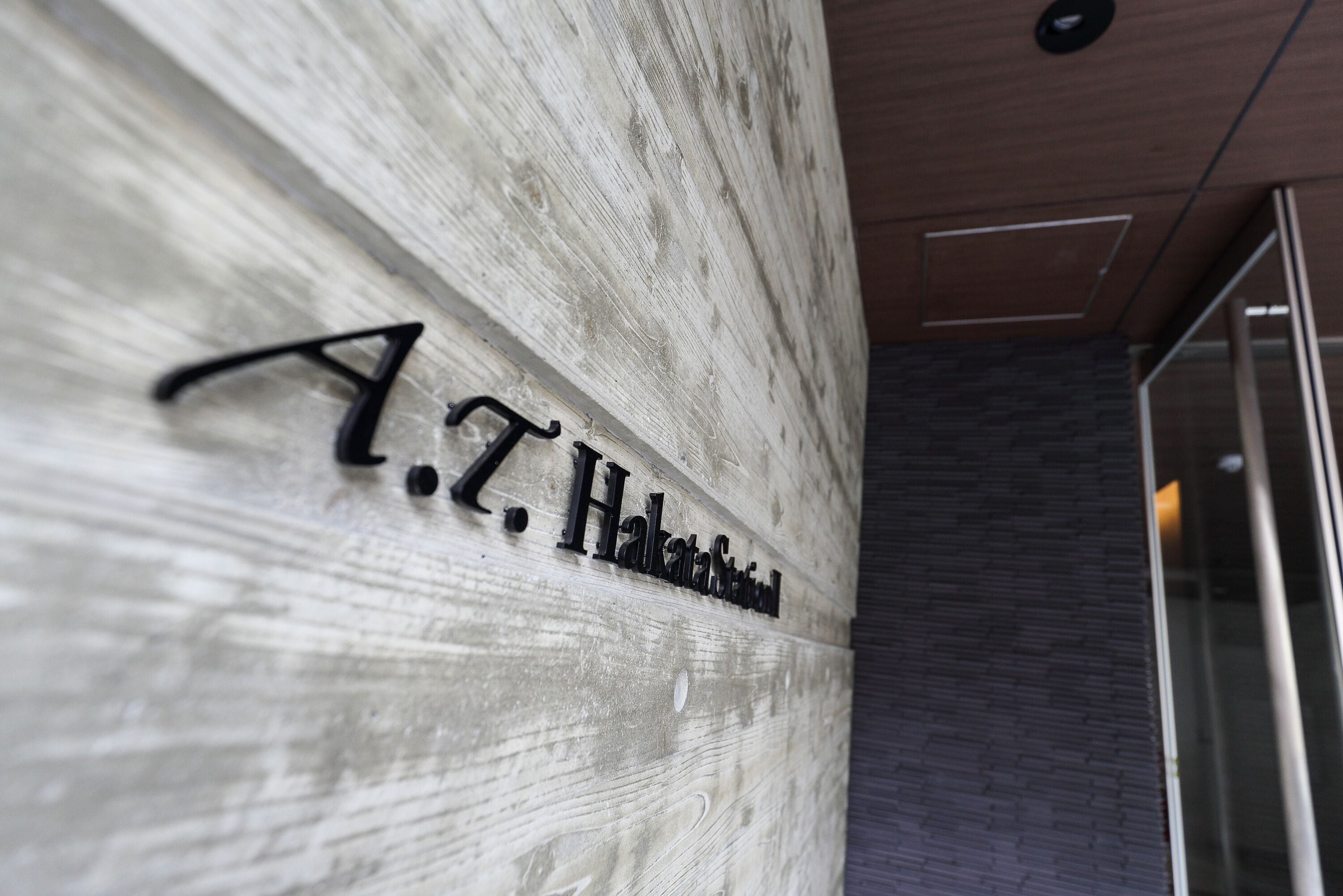 A sign with the text "A.T. Hakata Station" on a wooden wall.