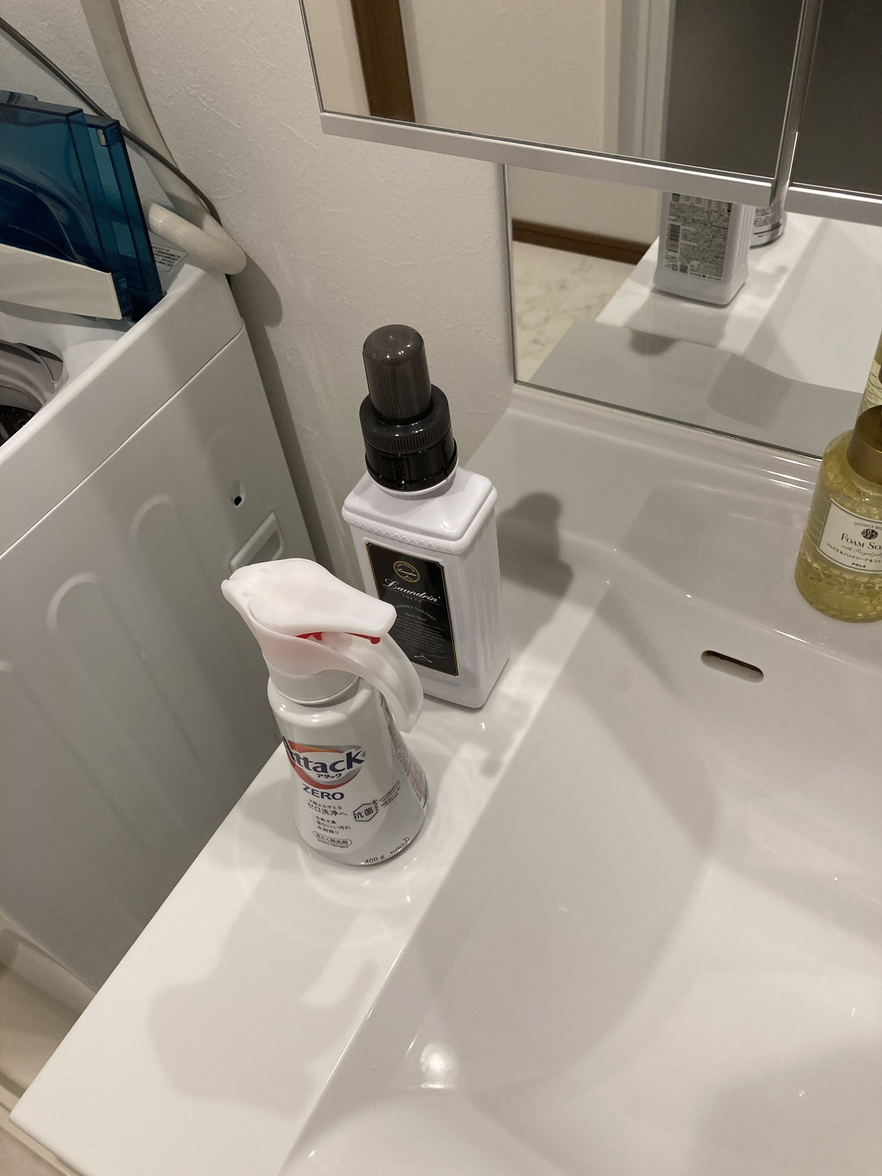 A bathroom sink with a white bottle of hand sanitizer, a small bottle of foam soap, and a mirror above the sink.