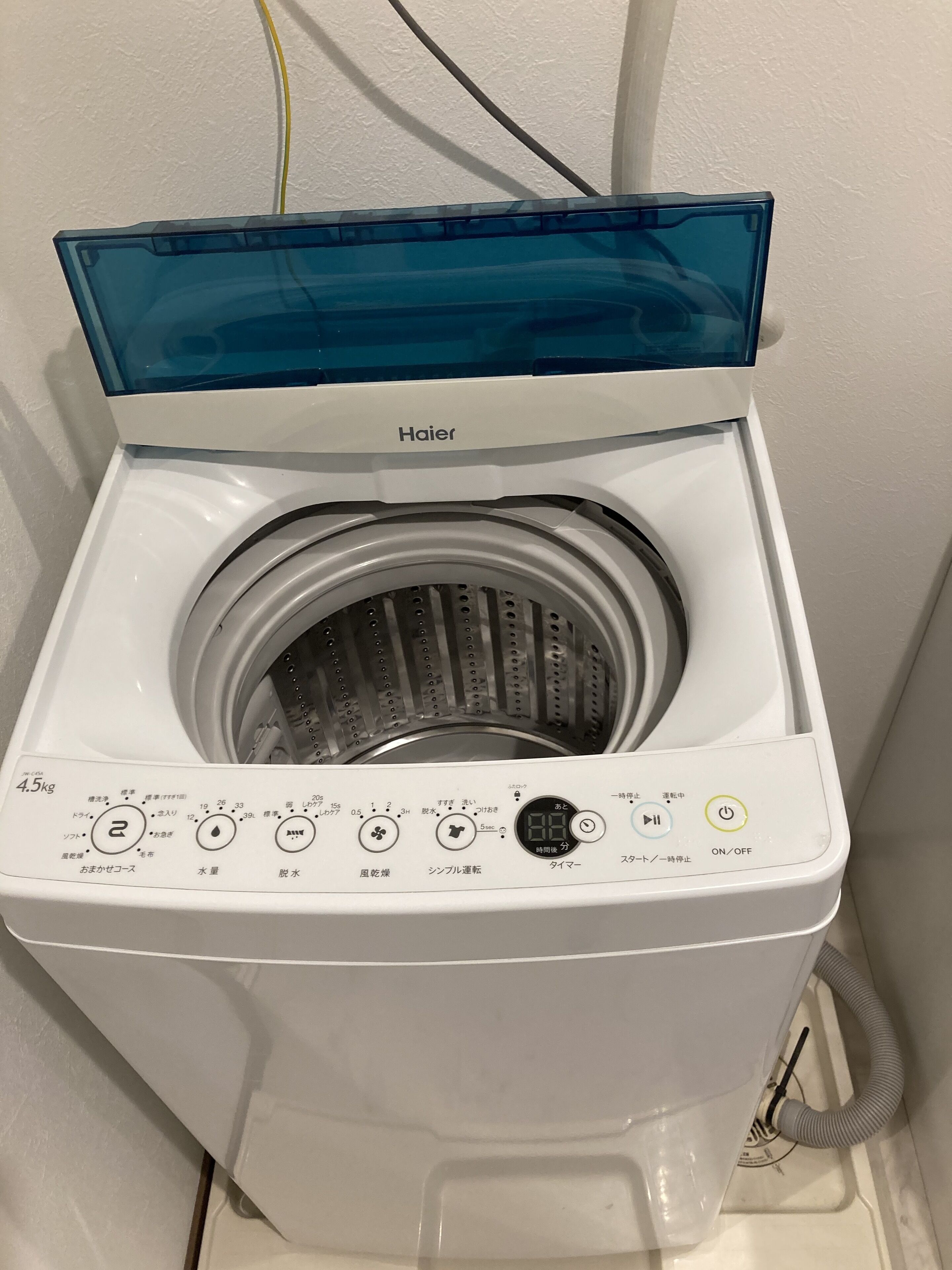A Haier front-loading washing machine with a transparent door, control panel, and a hose connection.
