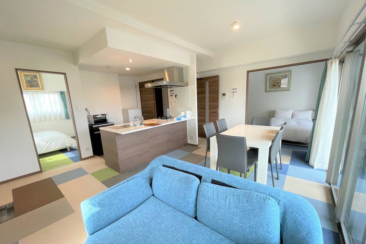 Una habitación de hotel moderna con sofá, una mesa de comedor con sillas, una zona de cocina y una cama.