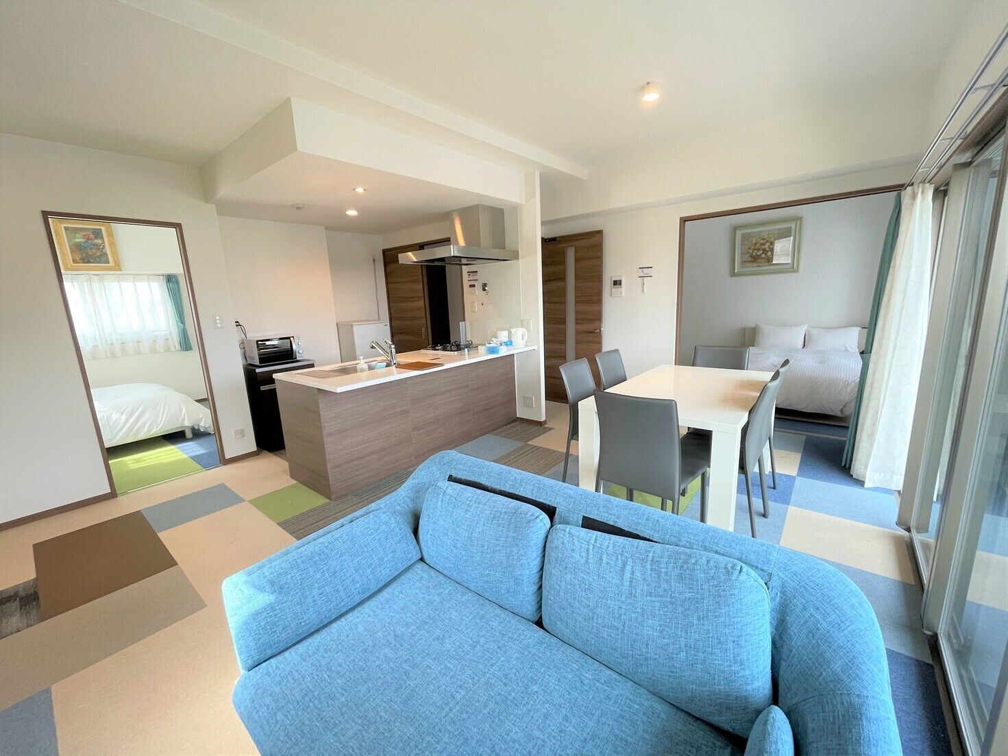 Ein modernes Hotelzimmer mit einer Couch, einem Esstisch mit Stühlen, einer Küchenzeile und einem separaten Schlafbereich.