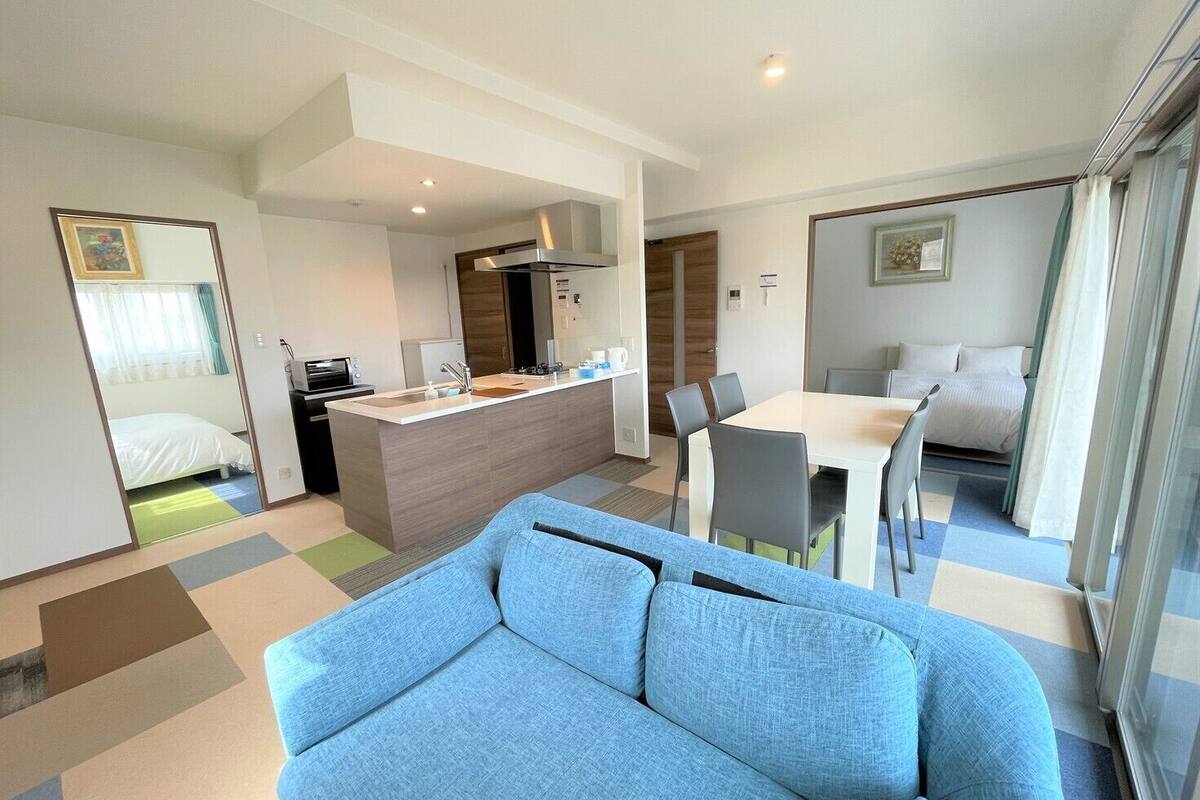 Une chambre d’hôtel moderne comprenant un canapé, une table à manger avec des chaises, un coin cuisine et une chambre à coucher séparée.