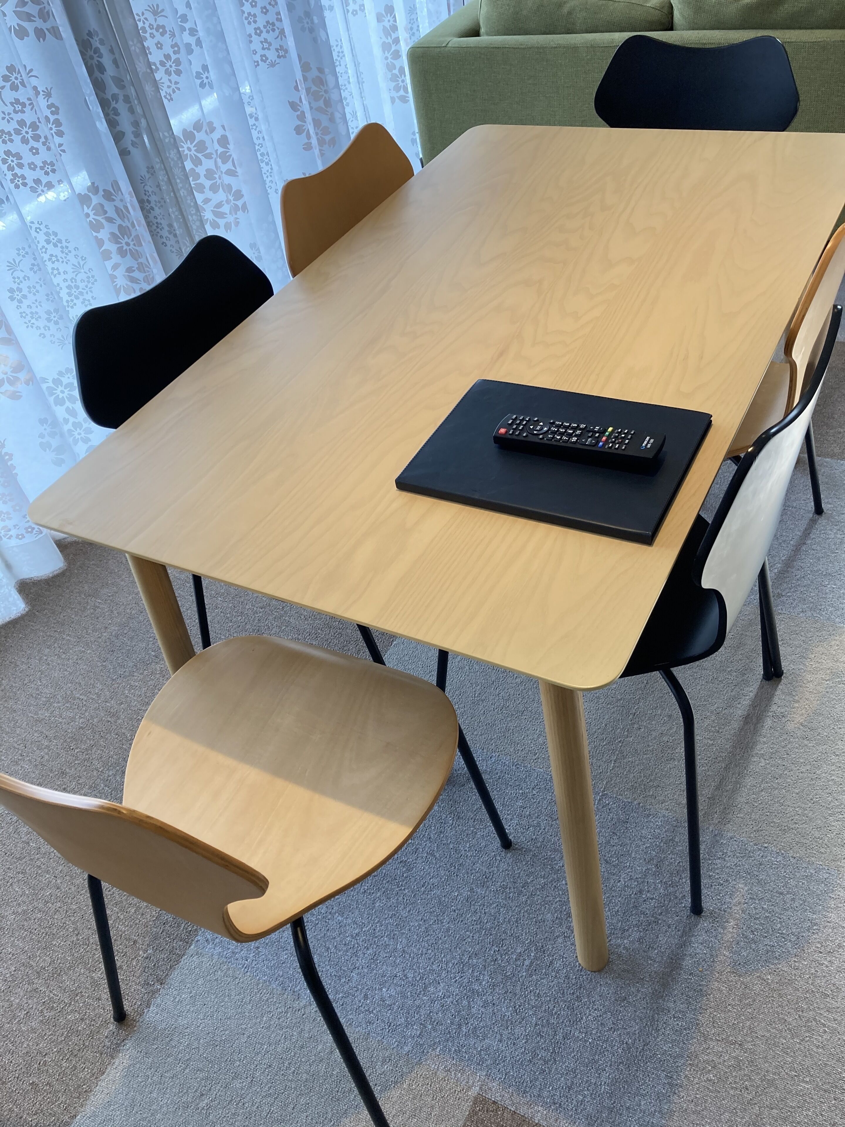 Une table à manger avec quatre chaises, une télécommande posée sur la table et un canapé vert à l’arrière-plan.