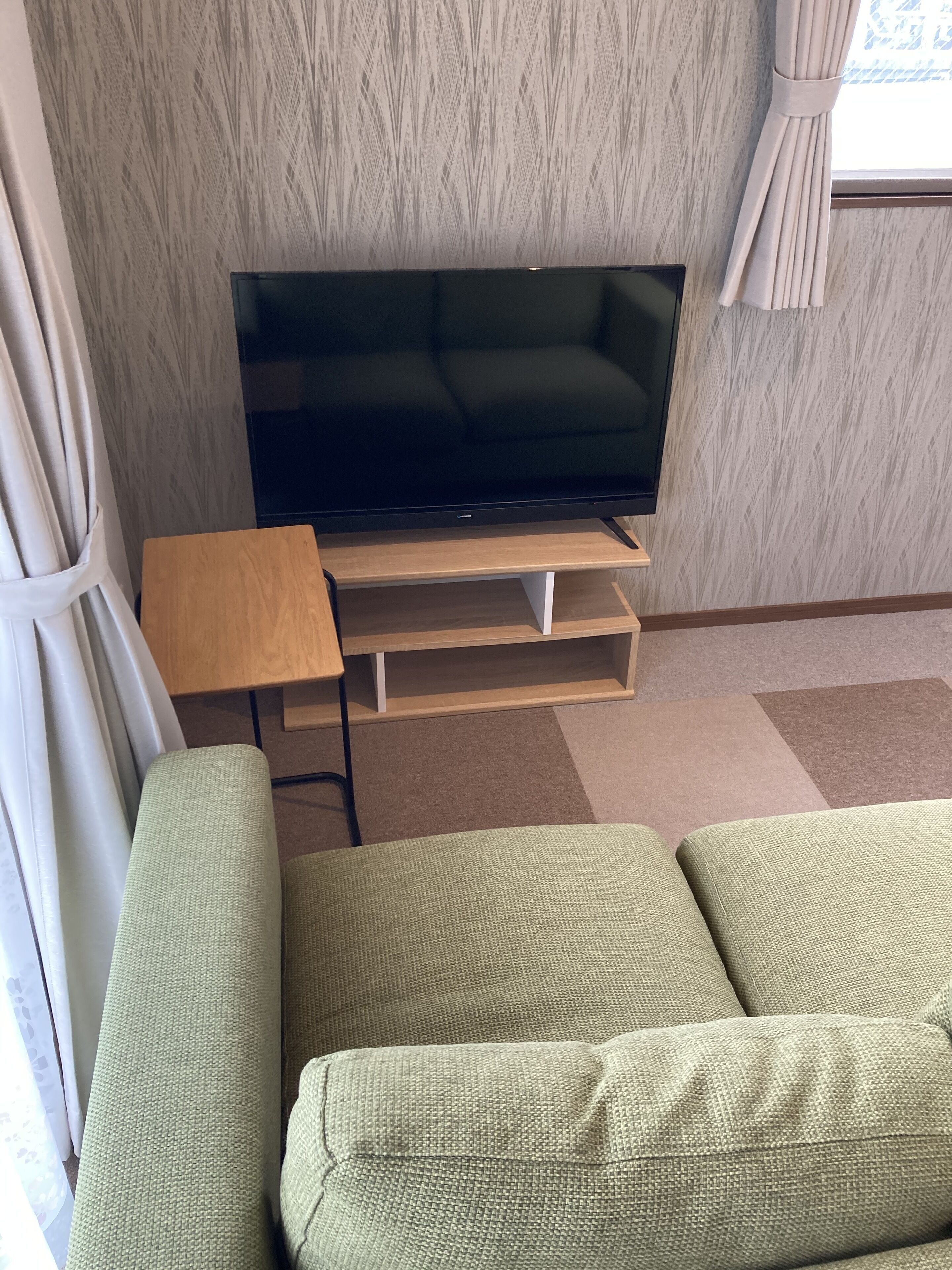 Una sala de estar con un televisor de pantalla plana sobre un soporte de madera, un sofá verde y una pequeña mesa de madera.