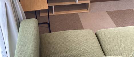 Una sala de estar con un televisor de pantalla plana sobre un soporte de madera, un sofá verde y una pequeña mesa de madera.