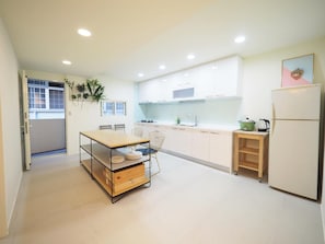 A modern kitchen with white cabinets, a wooden table with chairs, a refrigerator, and a window with blinds. - Near StayReal Location (Taipei)