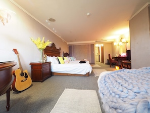 A hotel room with a bed, a guitar, a vase with flowers, a desk, and a chair. - Capital Family (Taipei)