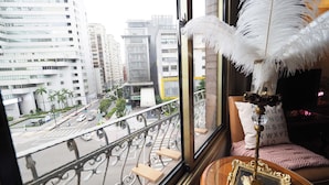 Une pièce avec vue sur le paysage urbain, grâce à une grande fenêtre, ornée d’une plume décorative et comprenant une petite table sur laquelle est posé un cadre photo.