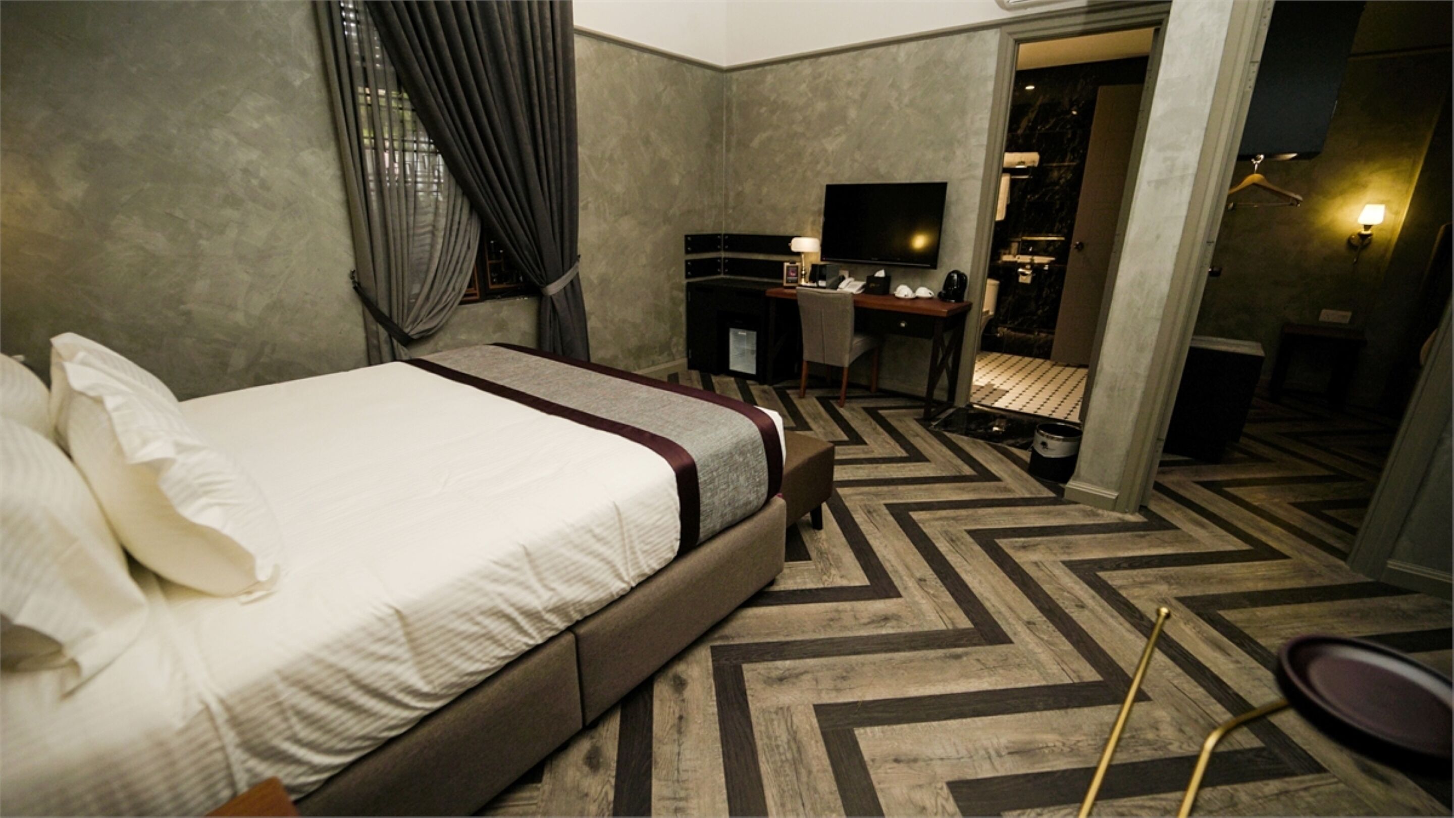 Habitación de hotel con una cama grande, un escritorio, un televisor y un baño visible a través de una puerta abierta.