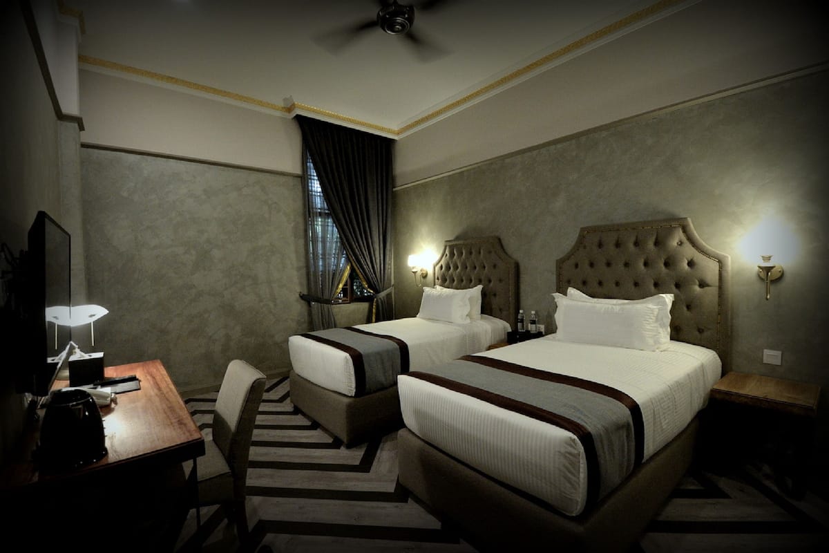 Ein Hotelzimmer mit zwei Betten, einem Schreibtisch, einem Stuhl und einem Deckenventilator.