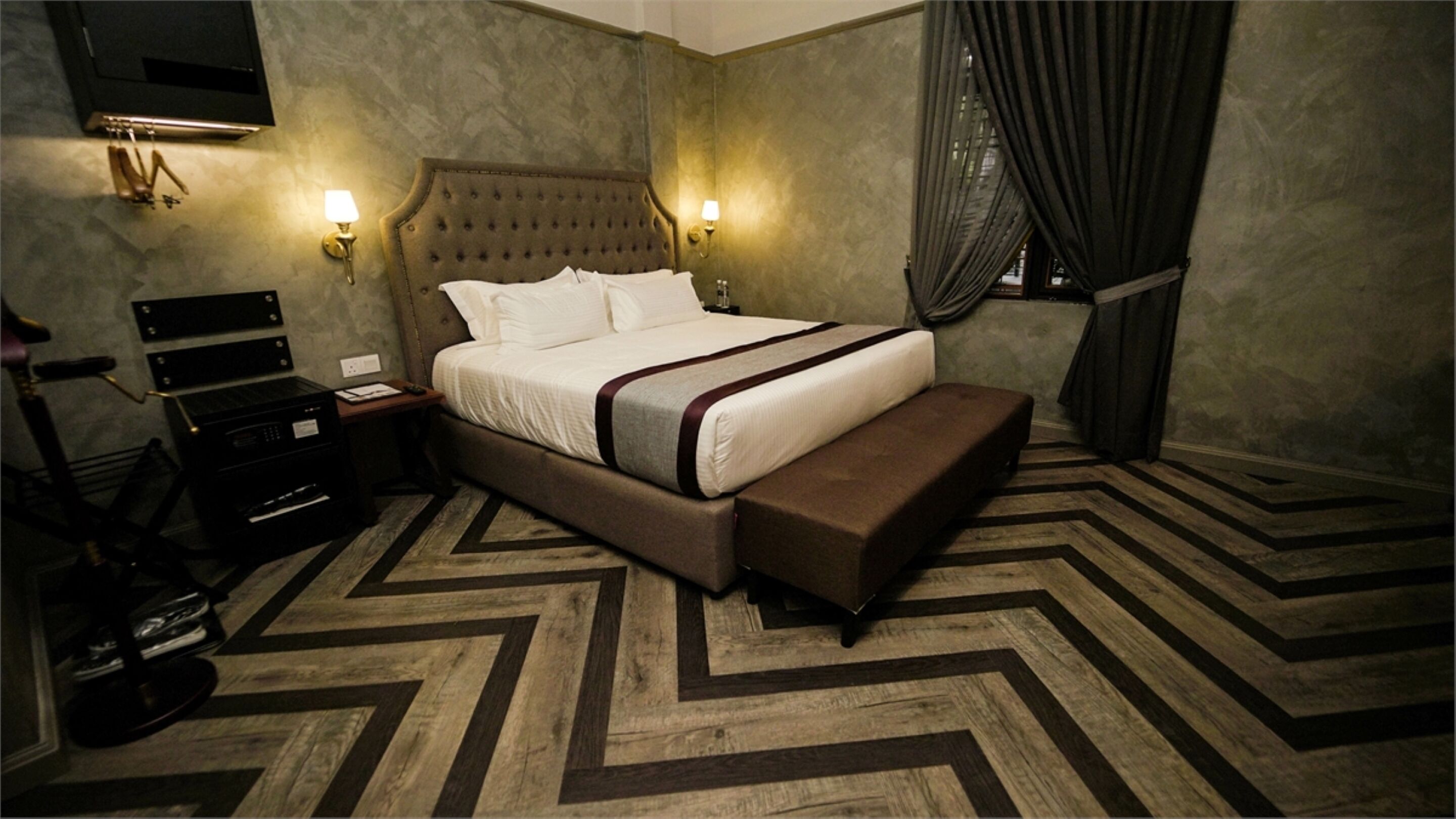 A hotel room with a large bed, a bench, a desk with a computer, and a TV.