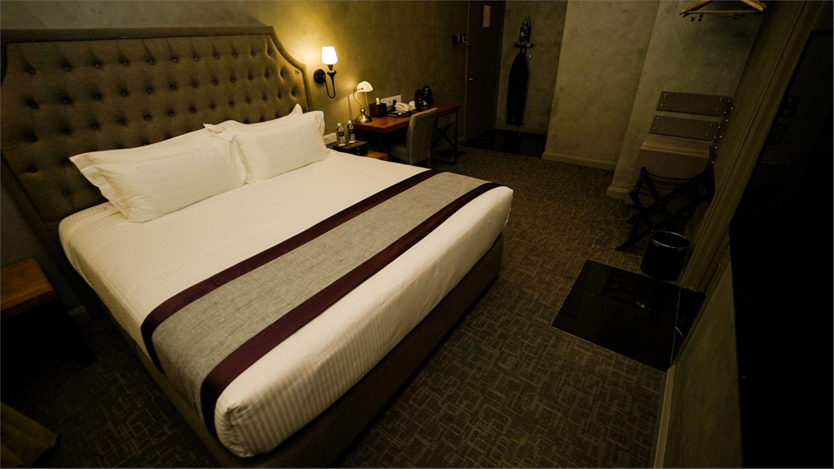 Una habitación de hotel con una cama grande, una mesita de noche con lámpara, un escritorio pequeño y un armario.