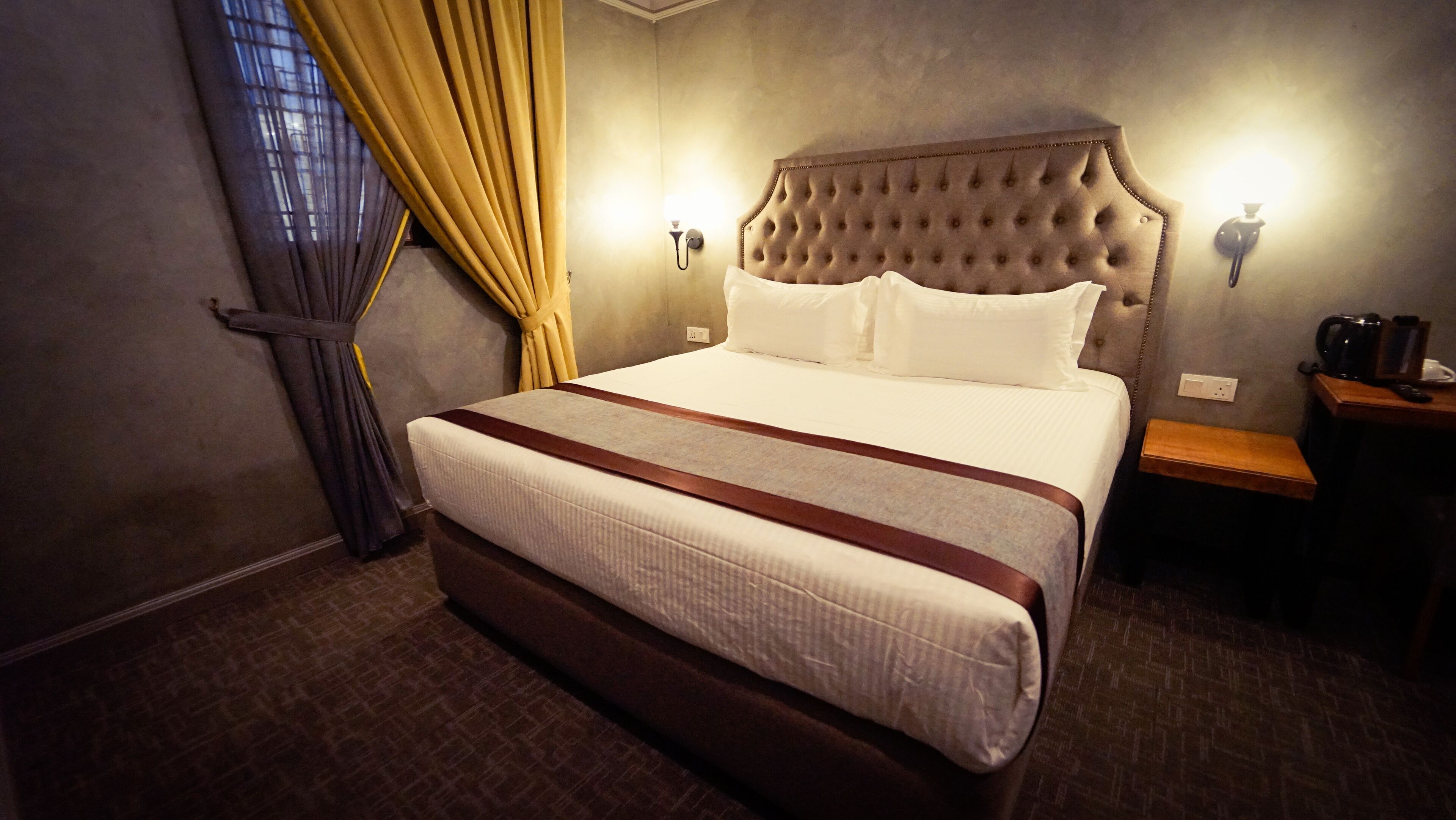 Una habitación de hotel con una cama grande, dos lámparas de noche, una mesita de noche de madera y una ventana con cortinas.