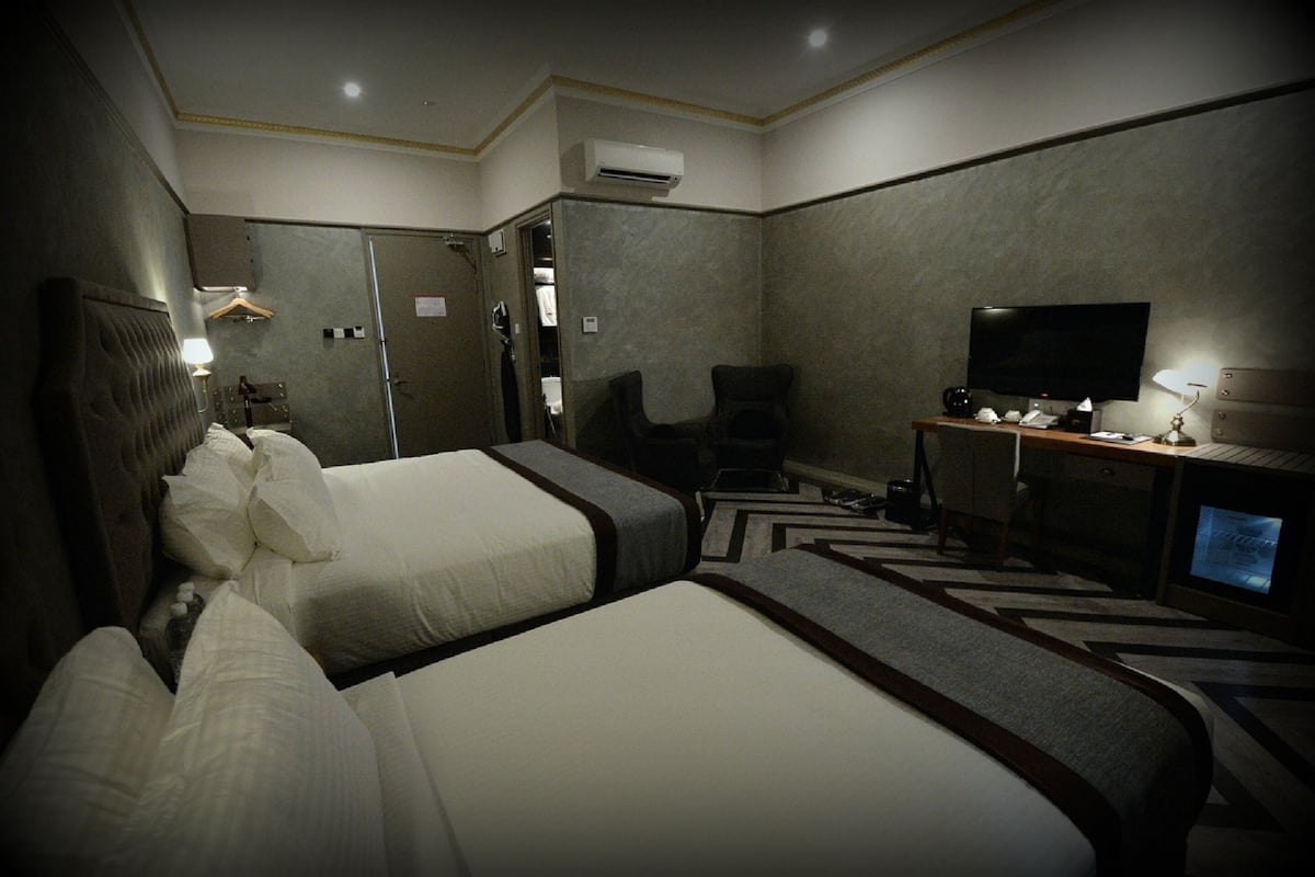Ein Hotelzimmer mit zwei Betten, einem Schreibtisch, einem Flachbildfernseher, einem Stuhl und einer Klimaanlage.