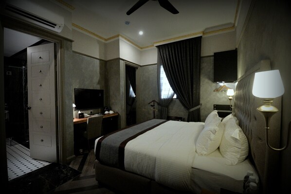 A hotel room with a bed, a desk, a TV, a lamp, and a bathroom with a shower and toilet.