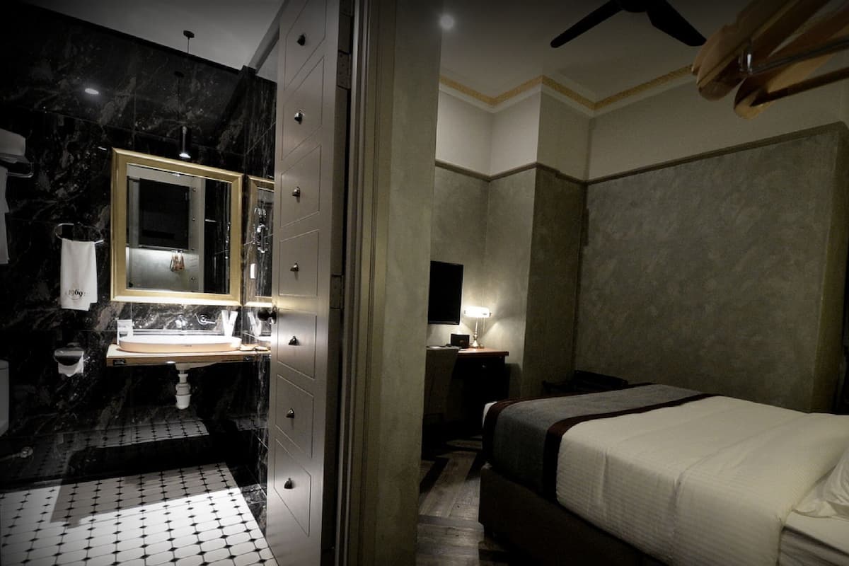 Ein Hotelzimmer mit Marmorbad, einem Bett mit weißer Bettwäsche und einem Nachttisch mit Lampe.