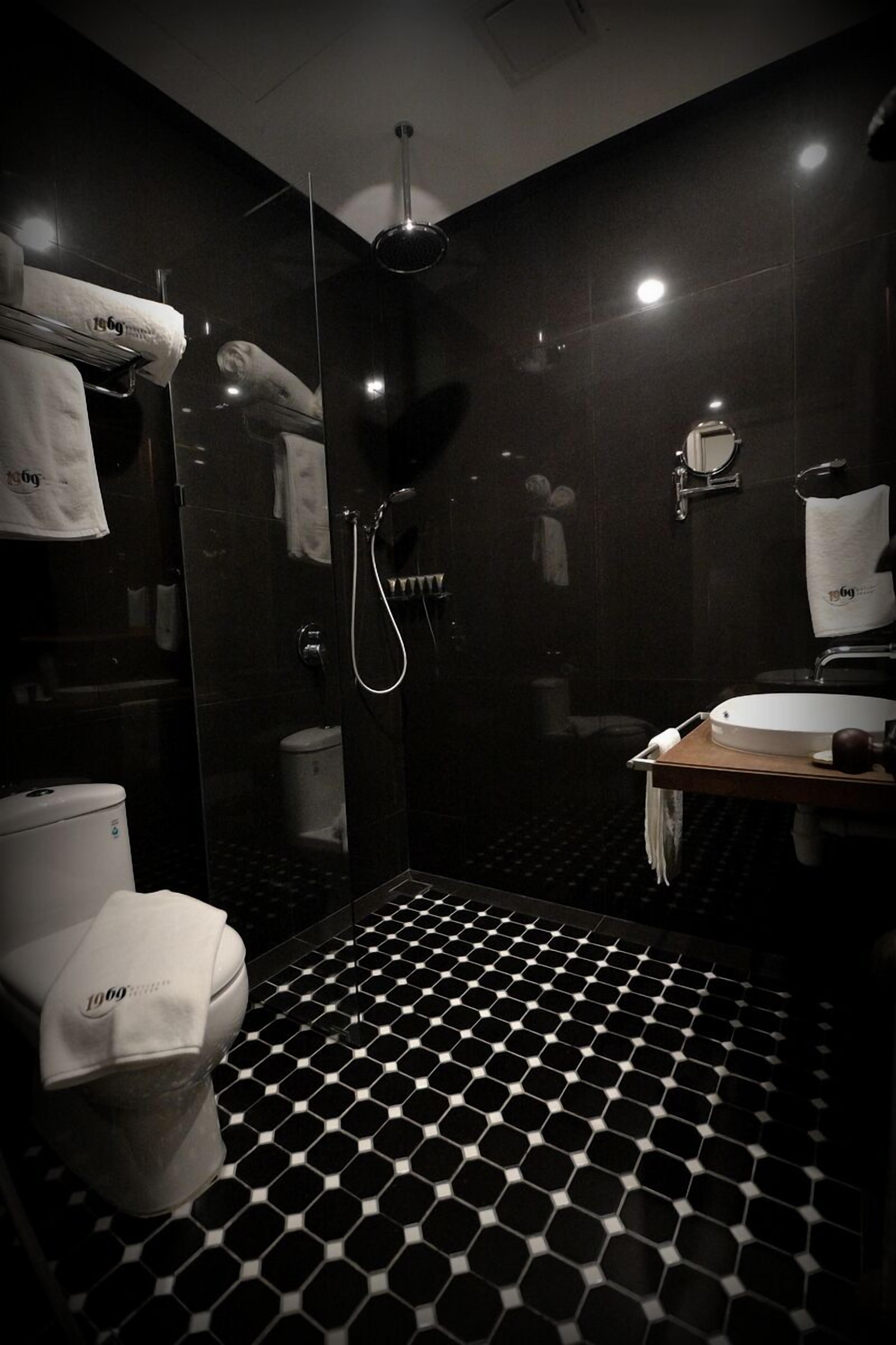 Un baño moderno con suelo de baldosas hexagonales blanco y negro, ducha con cerramiento de vidrio, inodoro y lavamanos con espejo.