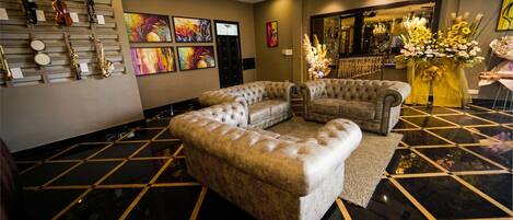 A lobby with a black and gold checkered floor, two tufted sofas, a wall-mounted violin rack, and colorful artwork.
