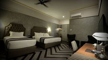 Ein Hotelzimmer mit zwei Betten, einem Schreibtisch mit Lampe, einem Sessel und einem Deckenventilator.